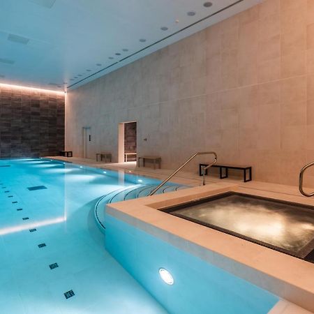 Citysuites 2 Aparthotel Manchester Zewnętrze zdjęcie The photo shows an indoor swimming pool area. The pool is a bright blue color and features smooth, tiled surfaces. On one side, there is a hot tub area with steps leading into it. The walls are made of light-colored stone, and there is ambient lighti