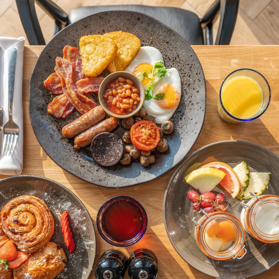 Citysuites 2 Aparthotel Manchester Zewnętrze zdjęcie The photo showcases a delicious breakfast spread. On a large, dark plate, there are items including crispy bacon, two fried eggs, baked beans, a grilled tomato, sautéed mushrooms, sausage links, and slices of black pudding. There's also a few pieces 