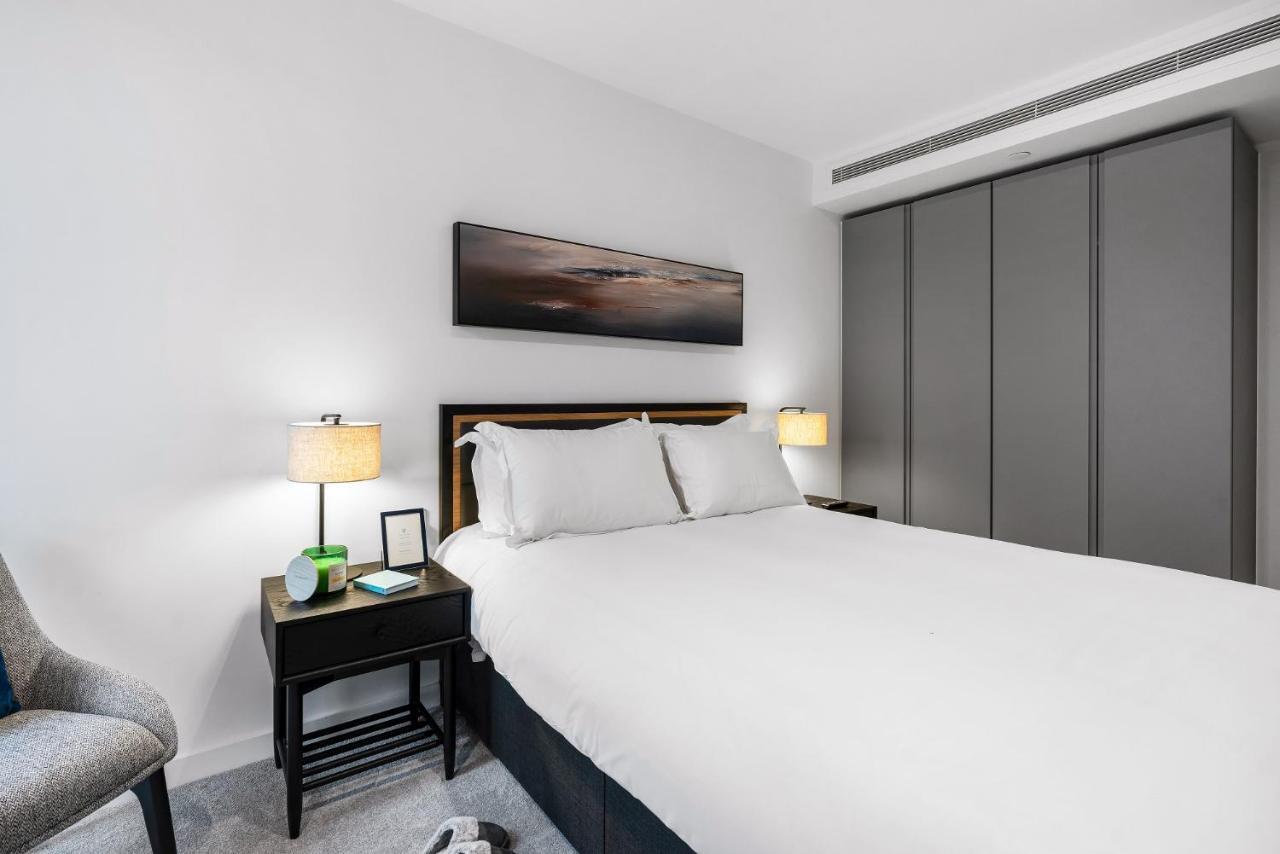 Citysuites 2 Aparthotel Manchester Zewnętrze zdjęcie The photo shows a modern bedroom with a neatly made bed featuring white linens and pillows. Flanking the bed are two bedside tables, each with a lamp providing soft lighting. There is a piece of artwork above the bed, which appears to depict a landsc