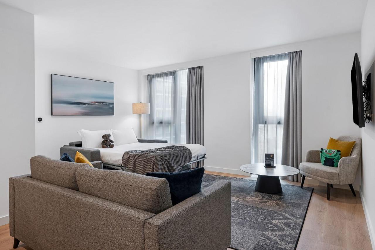 Citysuites 2 Aparthotel Manchester Zewnętrze zdjęcie The photo shows a modern living space that incorporates a cozy and inviting atmosphere. It features a light-colored couch with colorful cushions, positioned in front of a coffee table. There's a comfortable armchair nearby, and a throw blanket is dra