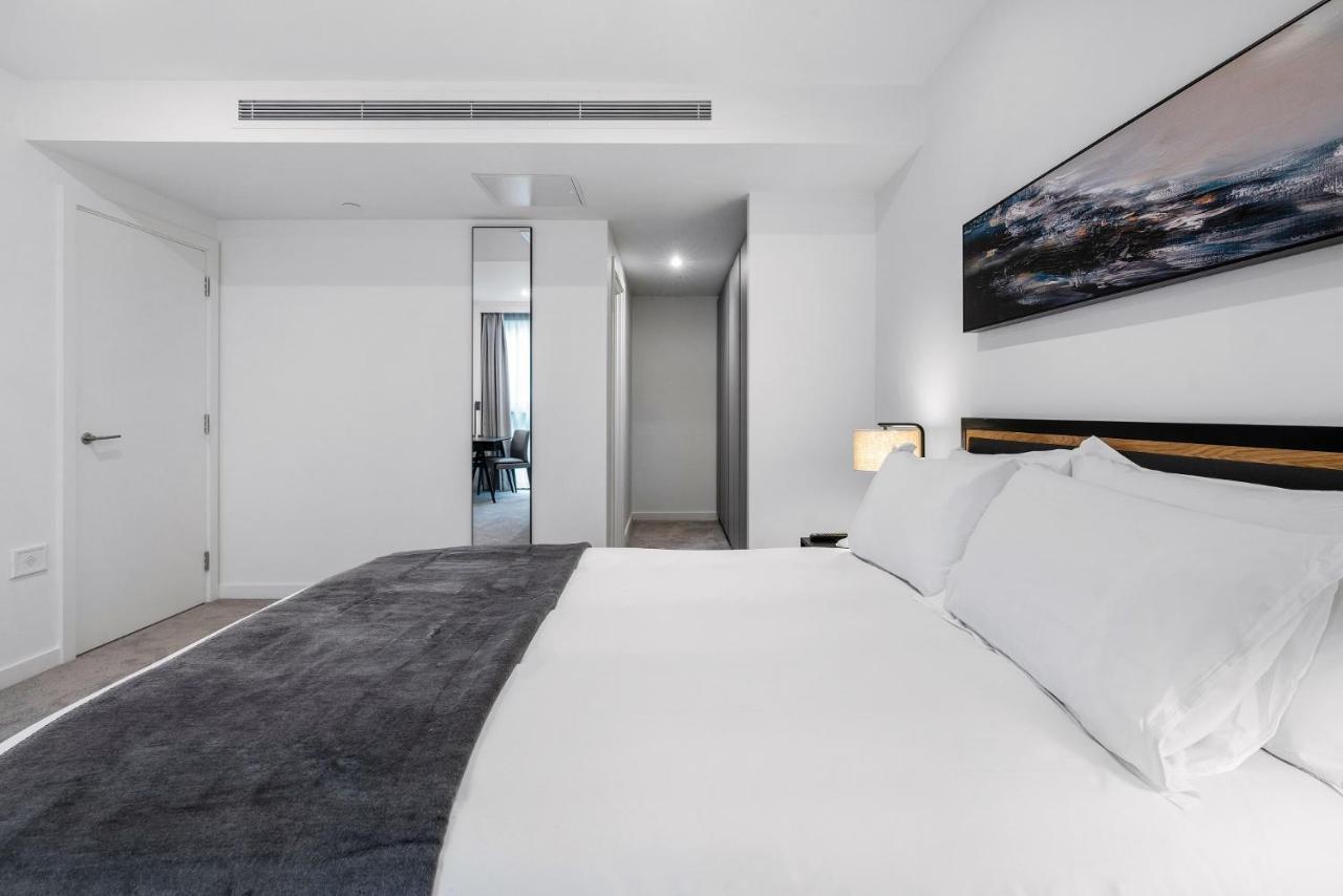 Citysuites 2 Aparthotel Manchester Zewnętrze zdjęcie The photo shows a modern bedroom with a minimalistic design. In the foreground, there is a neatly made bed with white linens and a dark gray throw blanket. To the side, there is a bedside lamp and a piece of abstract artwork on the wall above the bed