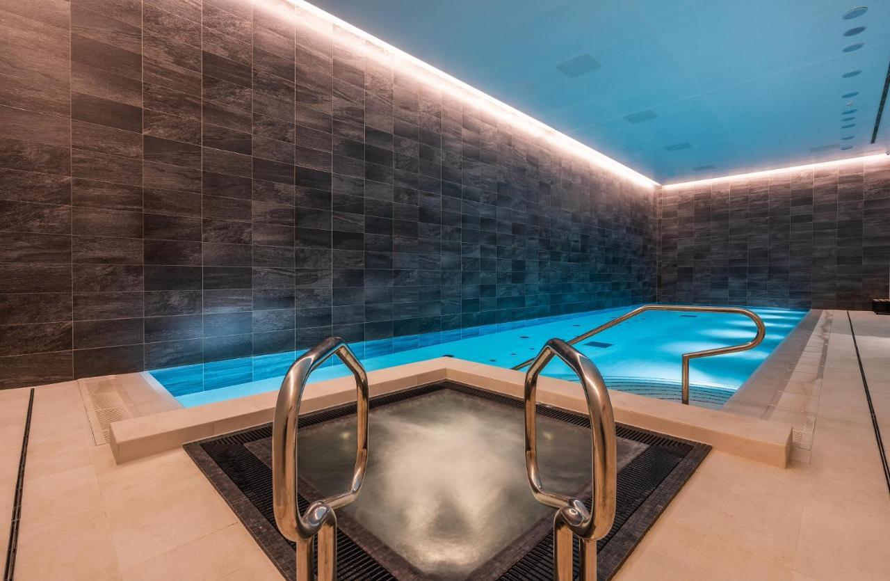 Citysuites 2 Aparthotel Manchester Zewnętrze zdjęcie The photo shows a modern indoor swimming pool area. The pool features a sleek, rectangular design with a beautiful blue water that seems illuminated. Surrounding the pool are dark, textured walls, adding to the elegant atmosphere. There are dual meta