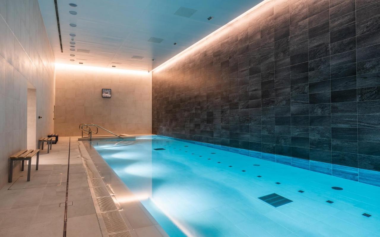 Citysuites 2 Aparthotel Manchester Zewnętrze zdjęcie The photo shows an indoor swimming pool area. The pool is illuminated with a soft blue light, creating a calming atmosphere. The walls are designed with dark tiles, and there is a lighter tiled area surrounding the pool. Ambient lighting is installed