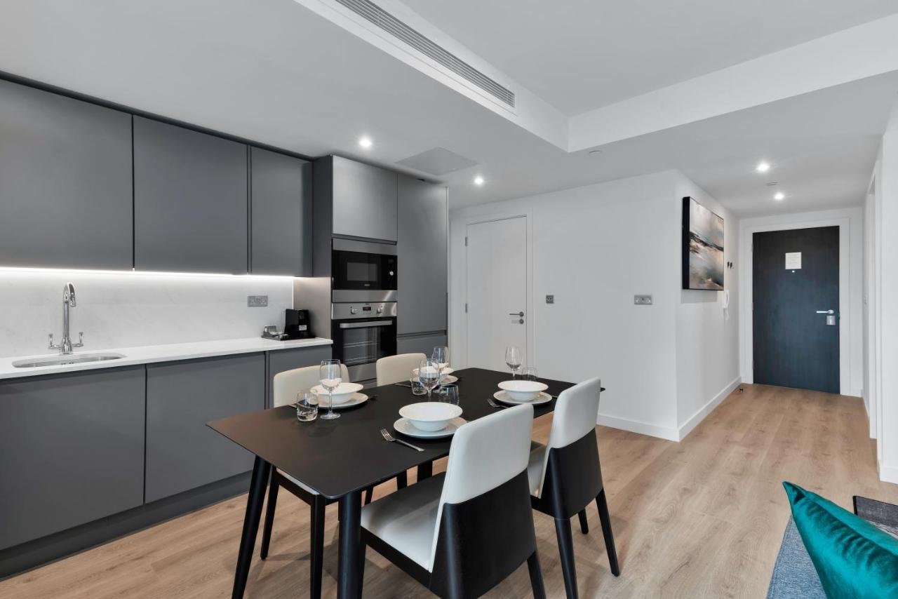 Citysuites 2 Aparthotel Manchester Zewnętrze zdjęcie The image shows a modern kitchen and dining area. The kitchen features sleek gray cabinets with a white countertop, and it is equipped with appliances such as a microwave. There’s a dining table set for four, with white plates and glasses ready. The 