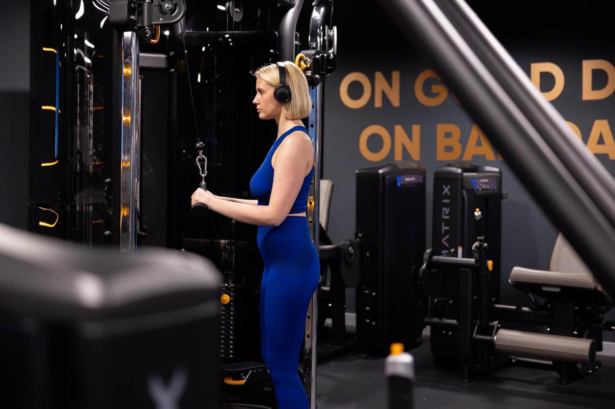 Citysuites 2 Aparthotel Manchester Zewnętrze zdjęcie The photo shows a woman working out in a gym. She is wearing a blue athletic outfit and headphones while using a gym machine. The background features various other gym equipment and a wall with the words "ON GOOD ON BAD" displayed prominently. The se