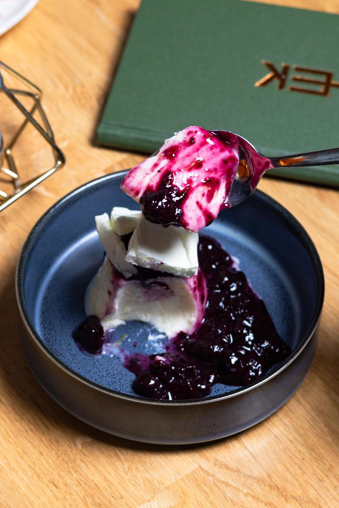 Citysuites 2 Aparthotel Manchester Zewnętrze zdjęcie The photo shows a serving of dessert, likely a type of panna cotta or a creamy custard, partially dished out and accompanied by a rich berry sauce, possibly made from blueberries or blackberries. A spoon with some of the dessert and sauce is hovering
